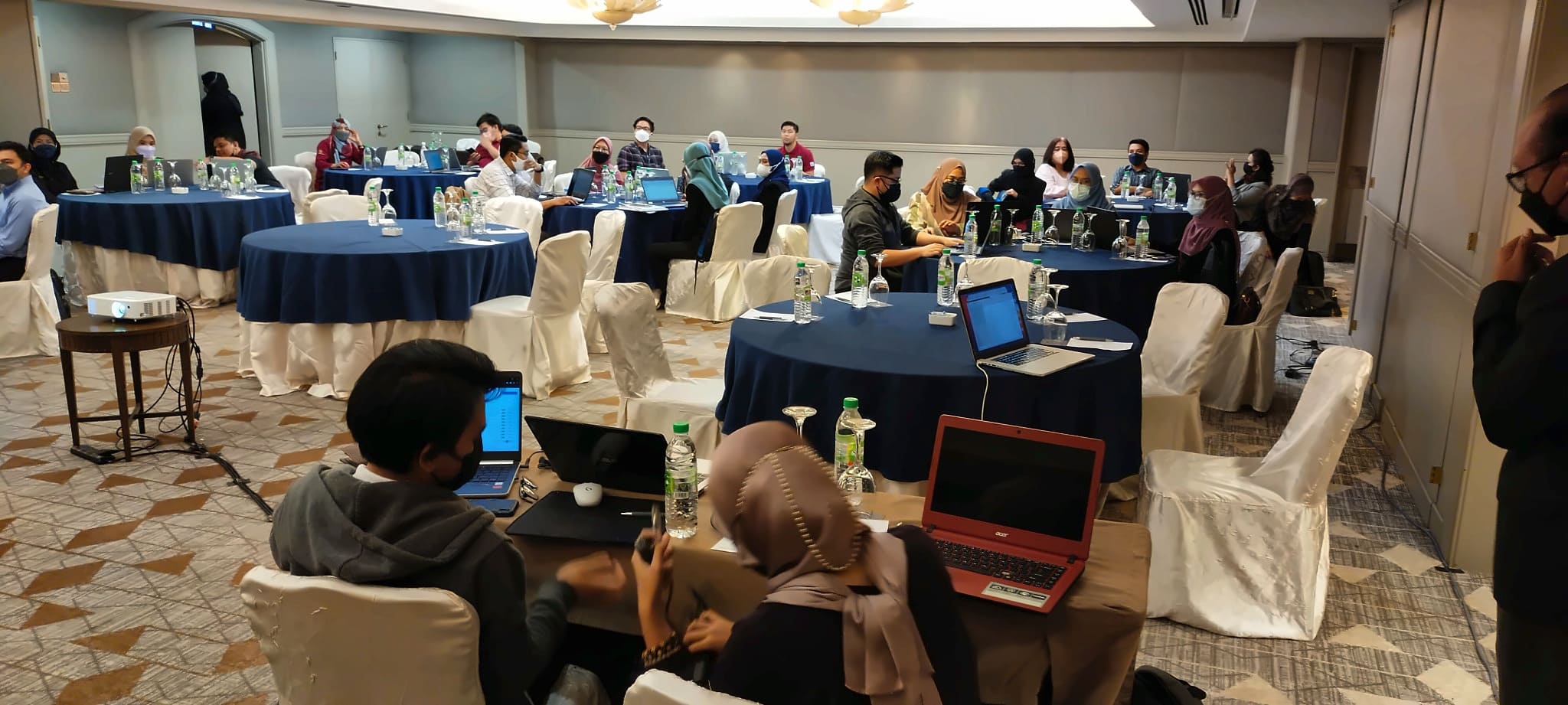 Workshop participants working in groups with laptops in a training hall