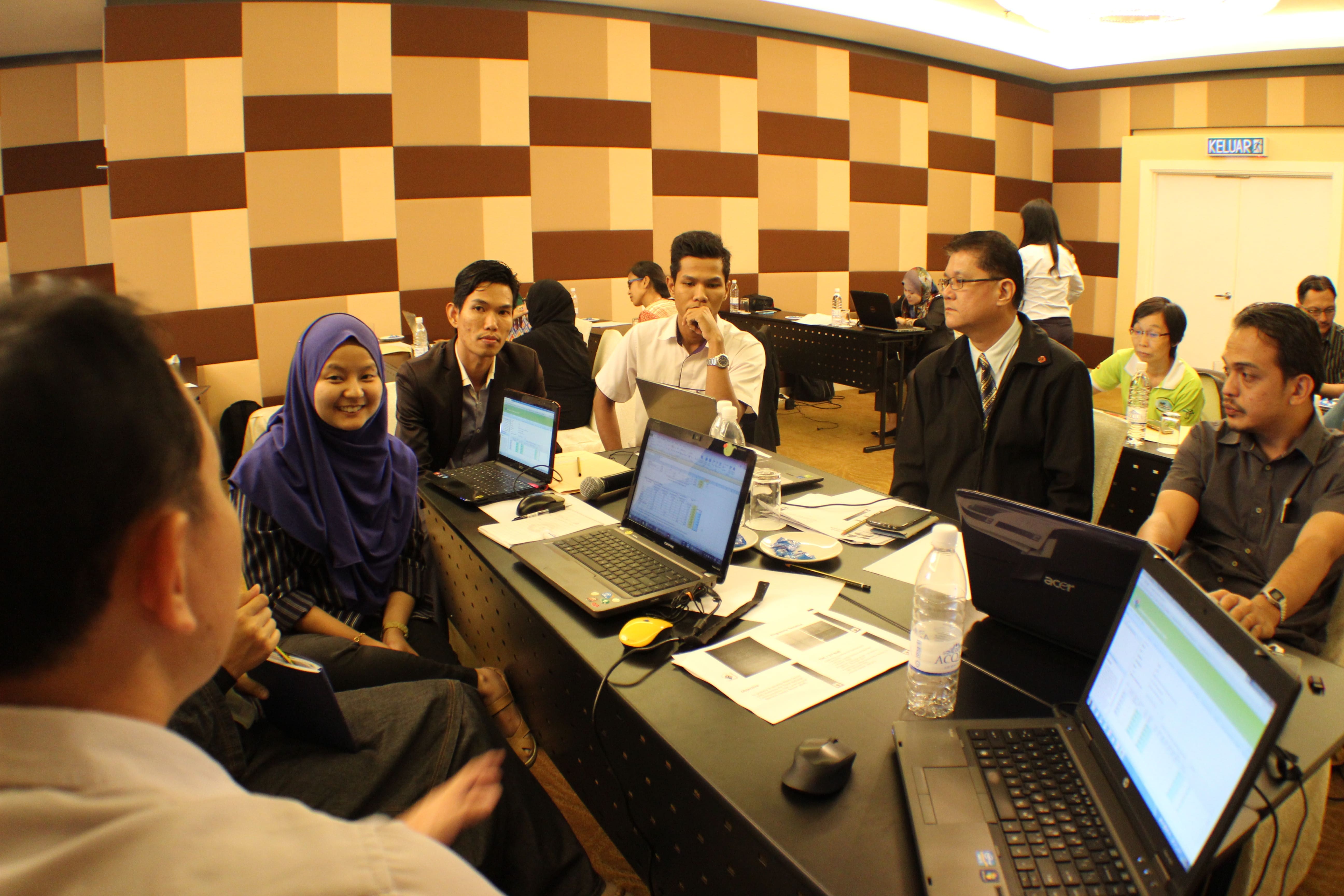 Workshop participants discussing software tasks around laptops displaying application screens
